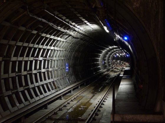 Looking down a stretch of the Transbay Tube, a bluish light illuminates the tunnel as it curves to the left.