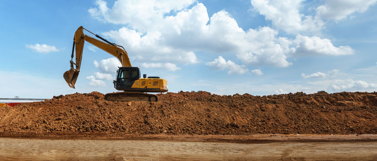 An excavator sits atop a large excess soil mound.