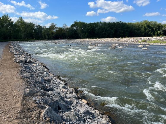 The shallow water running over rocks is turbulent. The water channel is lined with gray rocks.