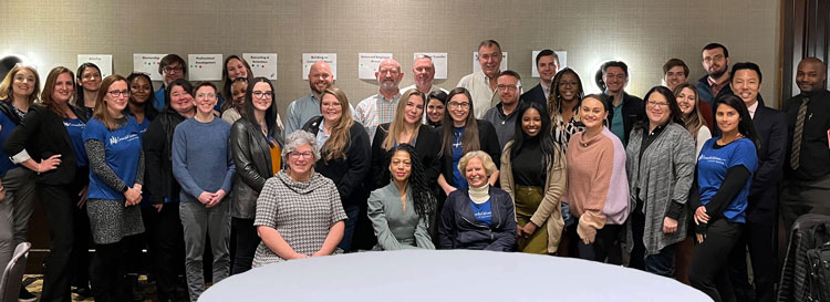 Diverse group of business professionals in a hotel conference room smile at the camera.