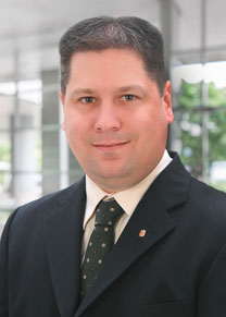 Dark-haired professional geologist in a suit poses for a headshot.