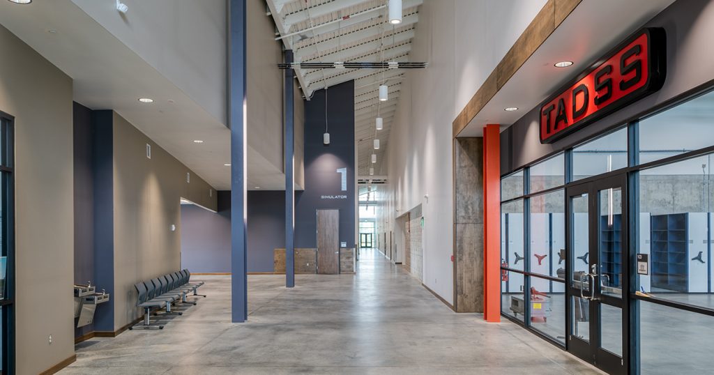 Inside of a building, facing the hallway with a seating area to the left and a room to the right.