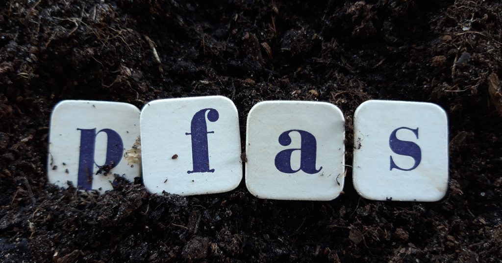 Four tiles spelling out PFAS surrounded by dirt.