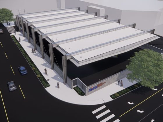 Aerial image of the white roof of a battery electric bus charging station building with streets on two sides, cars, and pedestrians.