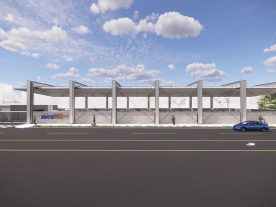 from the street looking at a white battery electric bus charging station building with cars on the street in front.
