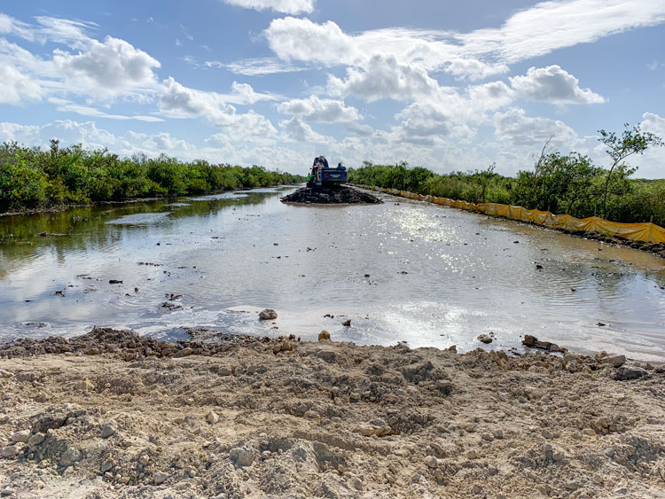 A piece of heavy equipment machinery sits on a mound of dirt, surrounded by water.