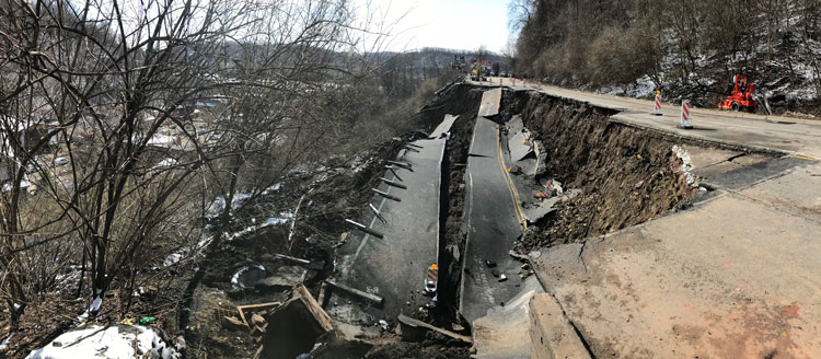 A landslide impacted half of the exiting highway causing extensive damage to the roadway and urban infrastructure downslope.