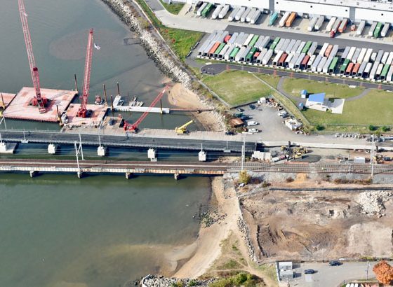 Arial image of a bridge construction area with two bridges crossing into a river towards the right.