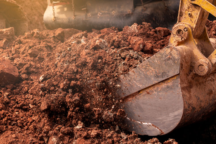 An excavator bucket is full of excess soil.