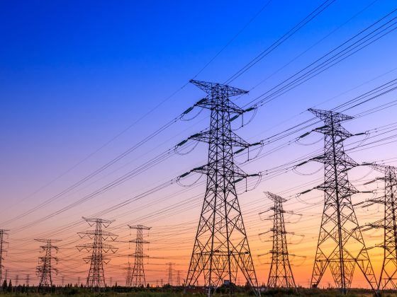High voltage electricity transmission towers against a colorful sunset.