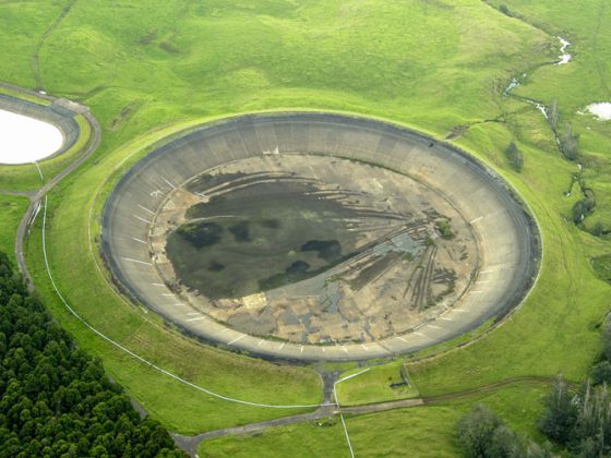 An aerial picture of a round, concave cement reservoir surrounded by grass fields on Hawaii Island.